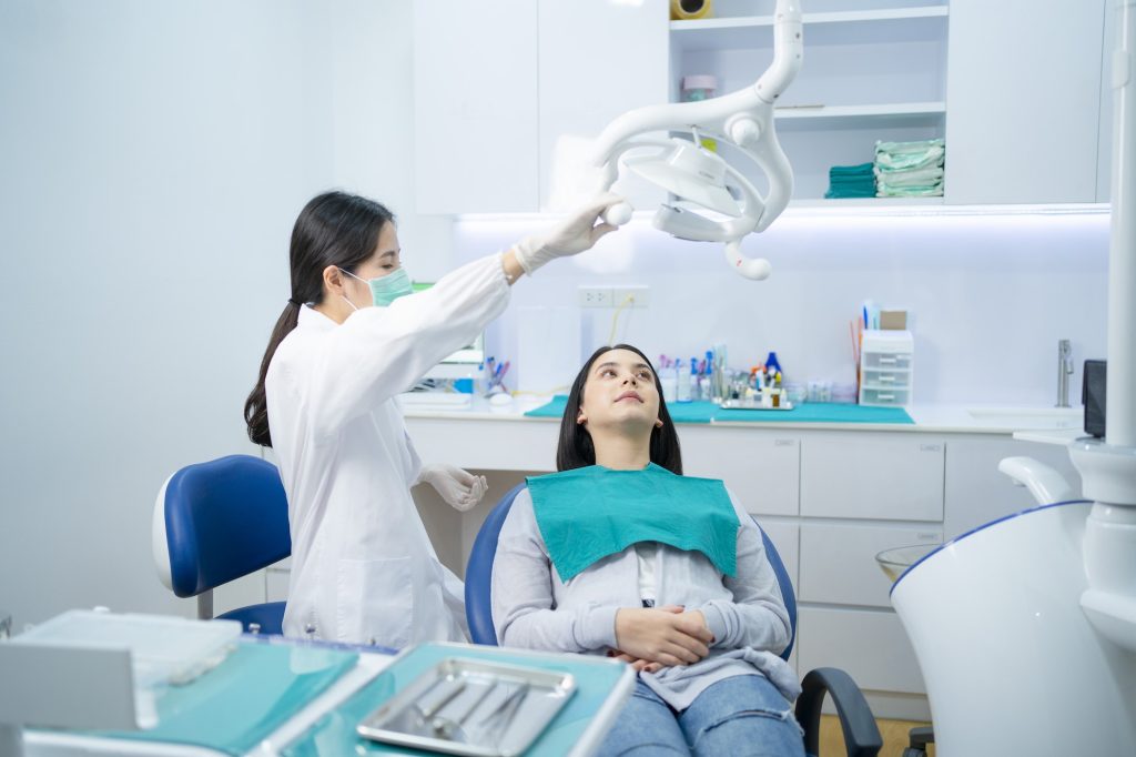 asian female dentist adjust dental surgical light then start checking or examining tooth of patient.jpg
